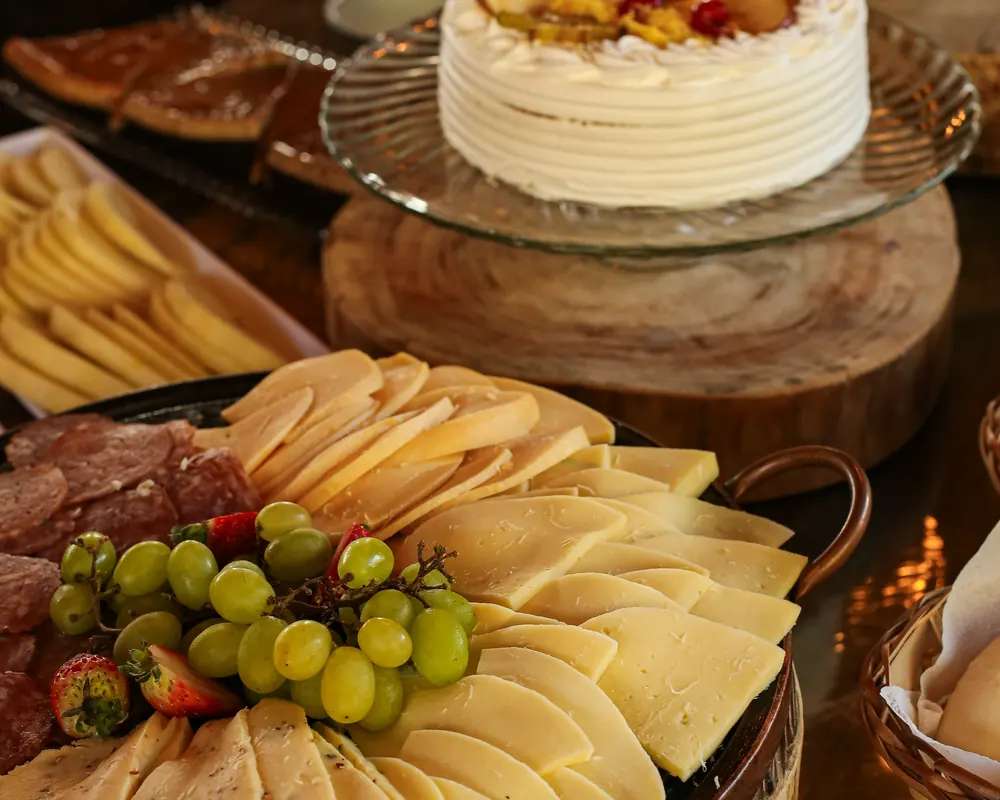 Tábua de queijos, frios, uvas e torta no buffet do café colonial.