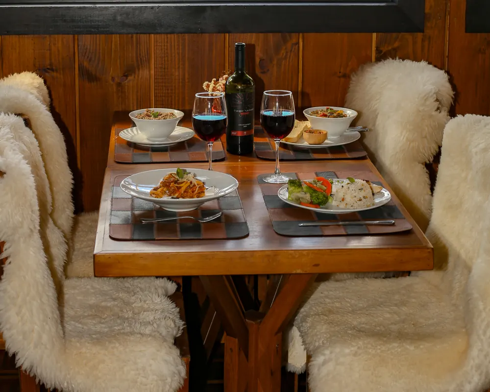Mesa com vinho e cadeiras de pelego junto à janela.