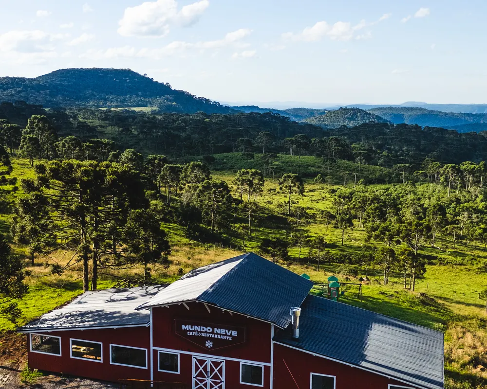 O celeiro vermelho entre araucárias, com as montanhas no horizonte.
