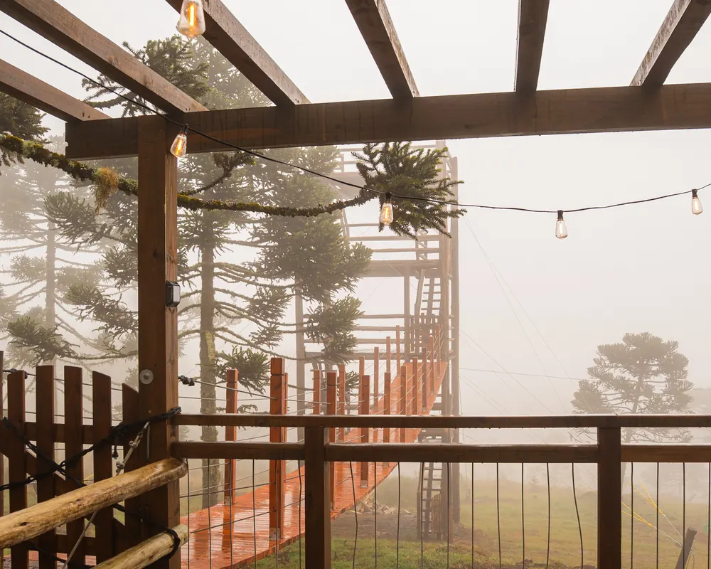Deck e ponte suspensa em meio à névoa da serra.
