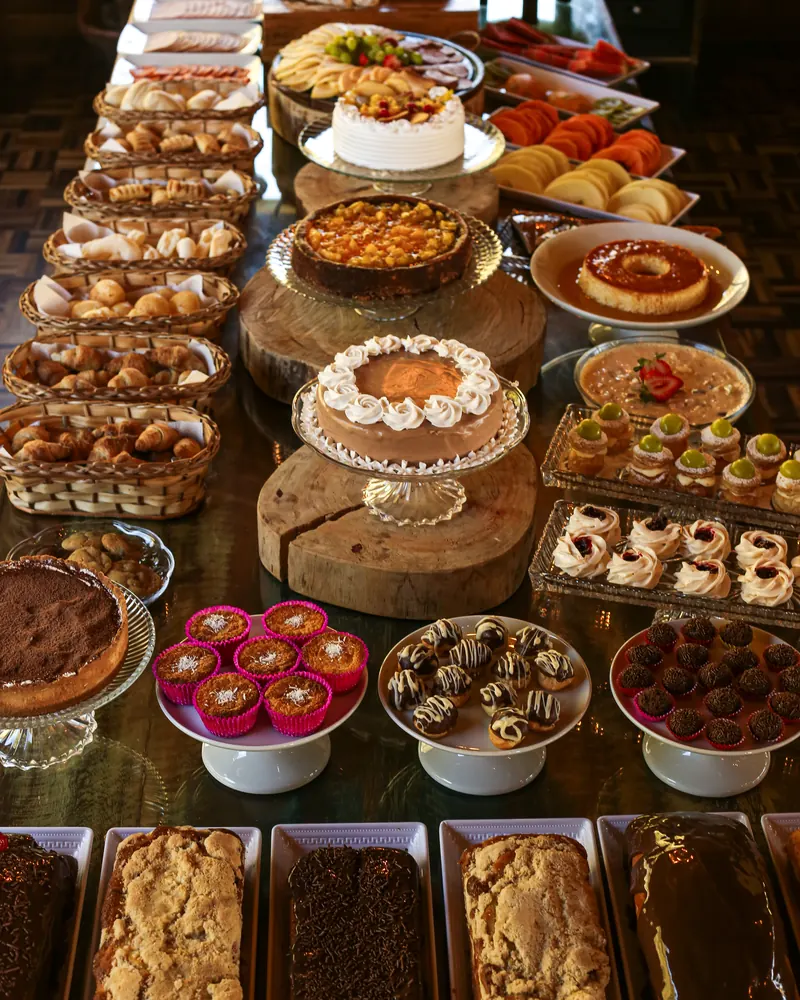 Mesa do café colonial com bolos, tortas, pudim, docinhos e pães.