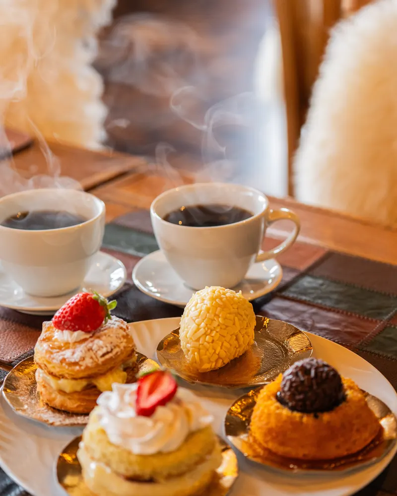 Café quente e doces servidos à mesa, com cadeiras de pelego.