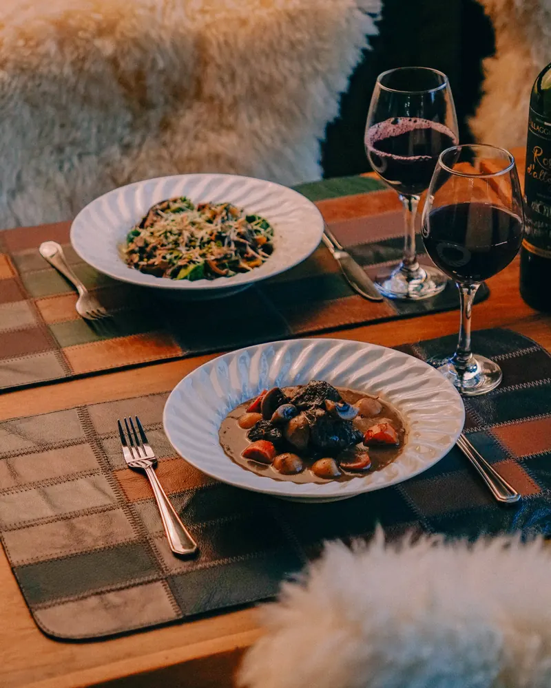 Mesa posta com pratos da casa e vinho, entre cadeiras de pelego.